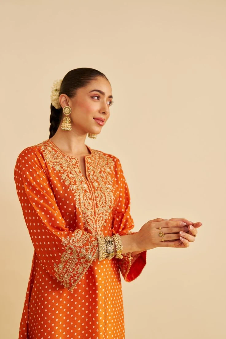 A model in an orange embroidered Indian outfit with traditional detailing